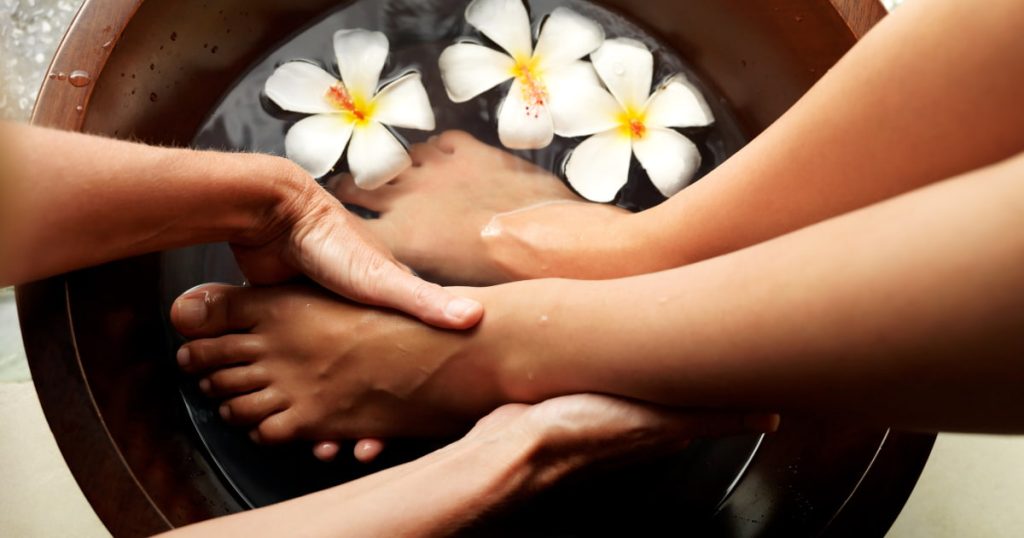 Deux pieds et deux mains dans un bassin d'eau avec des fleurs
