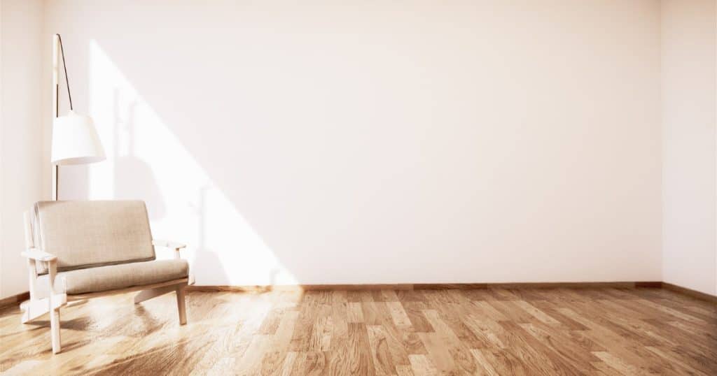 Fauteuil beige et lampe dans un coin de pièce lumineuse avec parquet en bois.