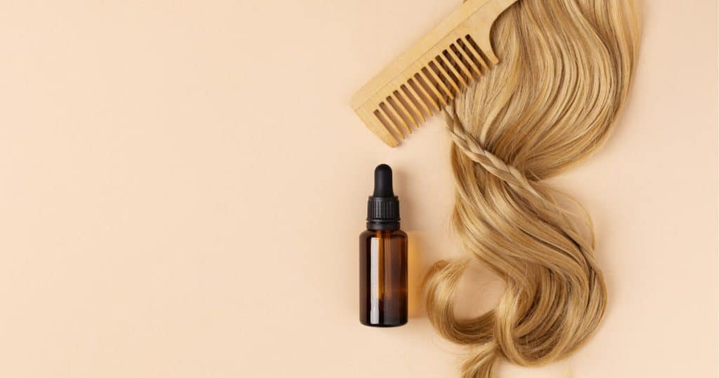 Cheveux blonds à coté d'un peigne et d'une petite bouteille de serum