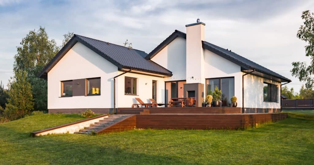 Maison contemporaine de plain-pied avec toit en pente, terrasse en bois et grandes baies vitrées donnant sur un jardin verdoyant.