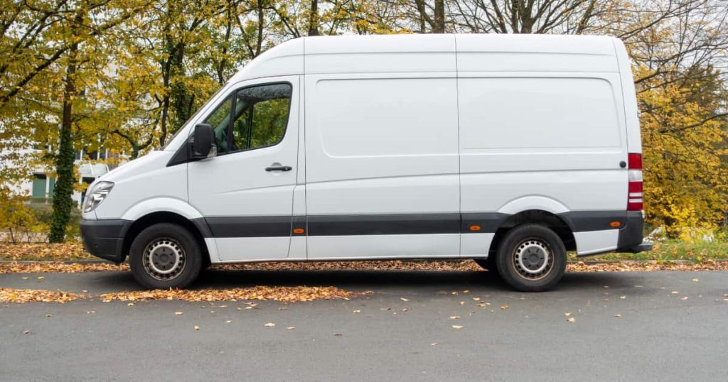 une camionnette lanche au bord de la route et des feuilles mortes par terre