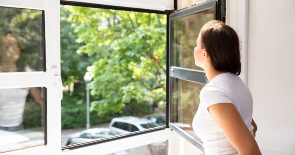 une femme qui regarde à travers une fenêtre ouverte