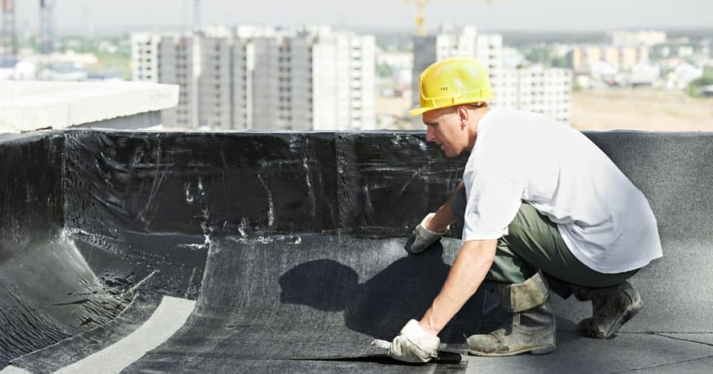 Application d’un revêtement d’étanchéité sur un toit-terrasse par un ouvrier en bâtiment.