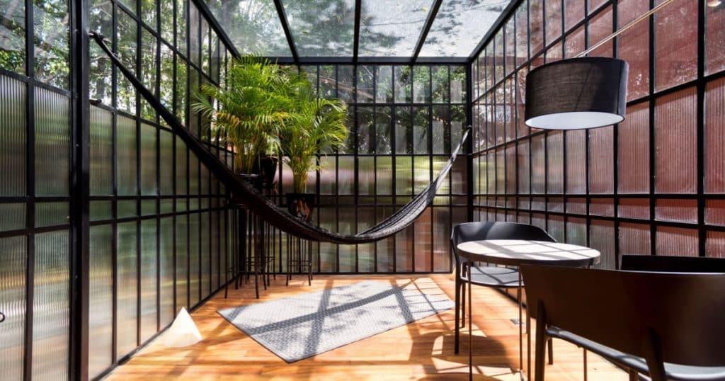 hamac, plantes, table et deux chaise dans une véranda vitrée à toit plat