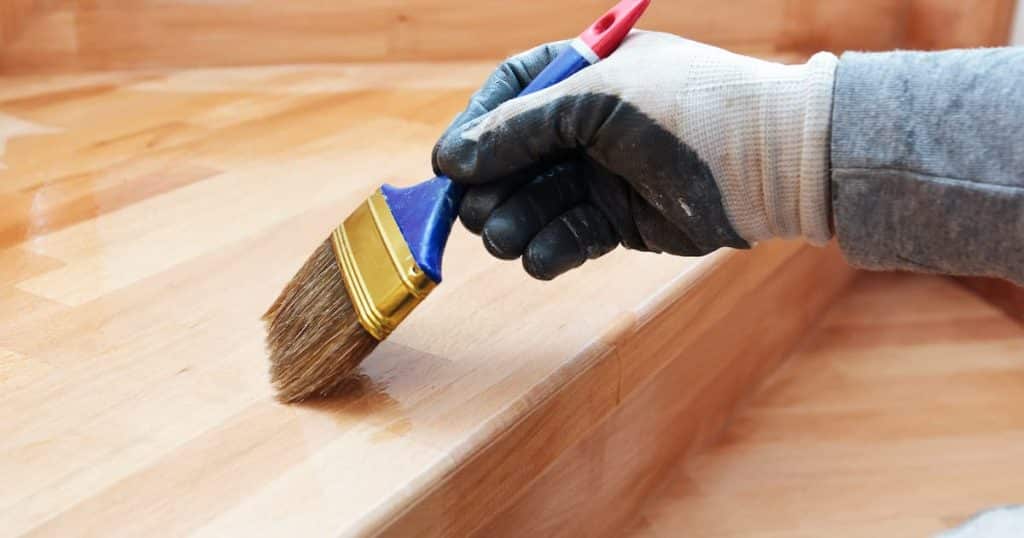 Une personne en train de vitrifier un escalier  avec un pinceau