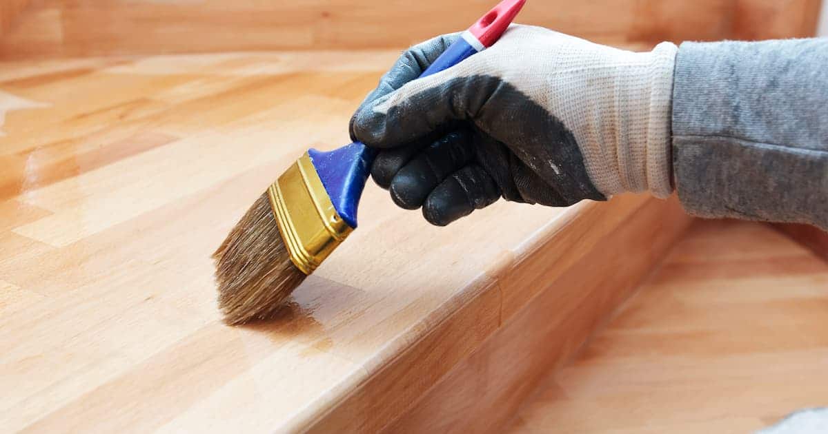 Un homme en train de vitrifier un escalier en bois avec un pinceau