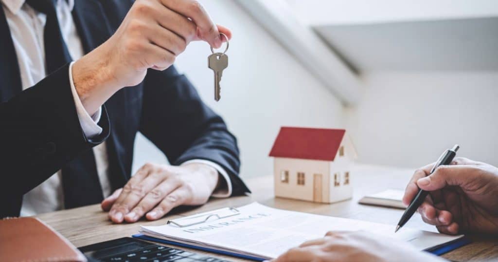 Un homme en costume tend les clés d'une maison à une personne en train de signer un document, d'achat ou de location. 