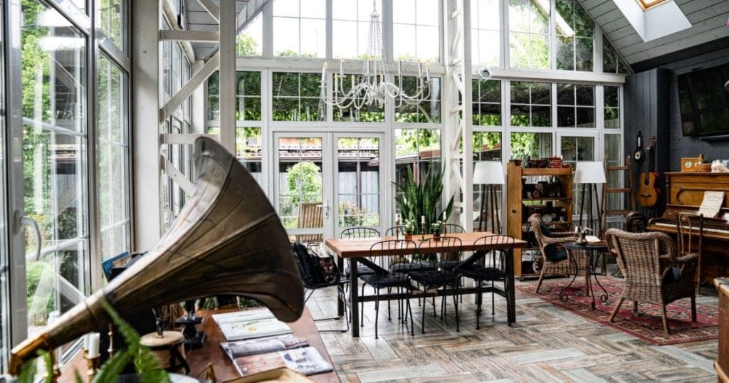 véranda vitrée aménagée avec une table, des chaises, et un instrument de musique