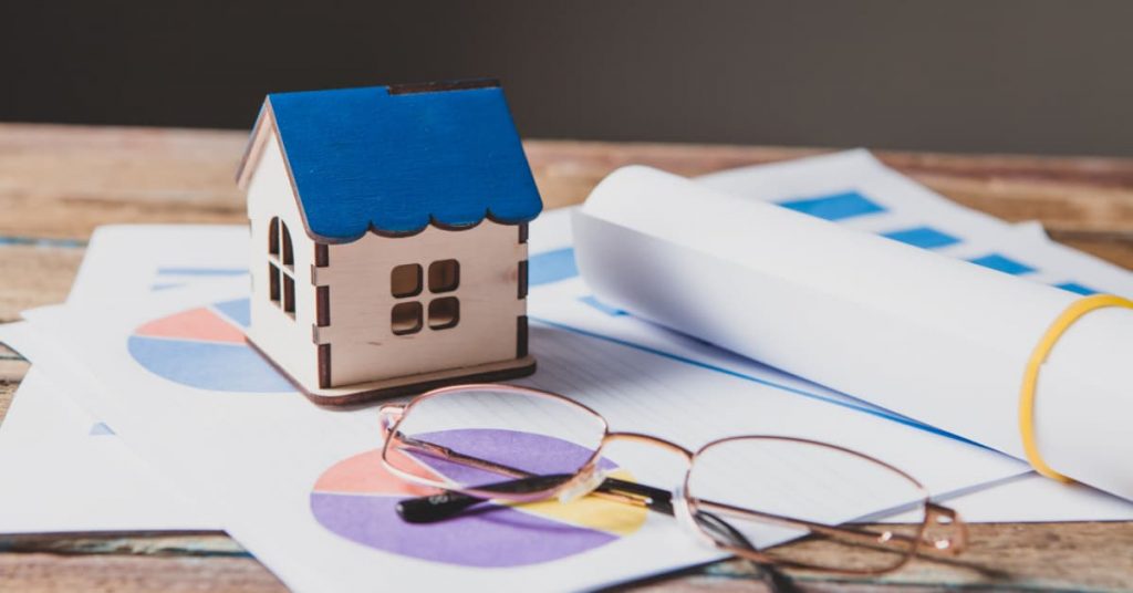 petite maison mignature en bois sur posé sur un bureau avec des documents analysant la performance énergétique d'un bâtiment