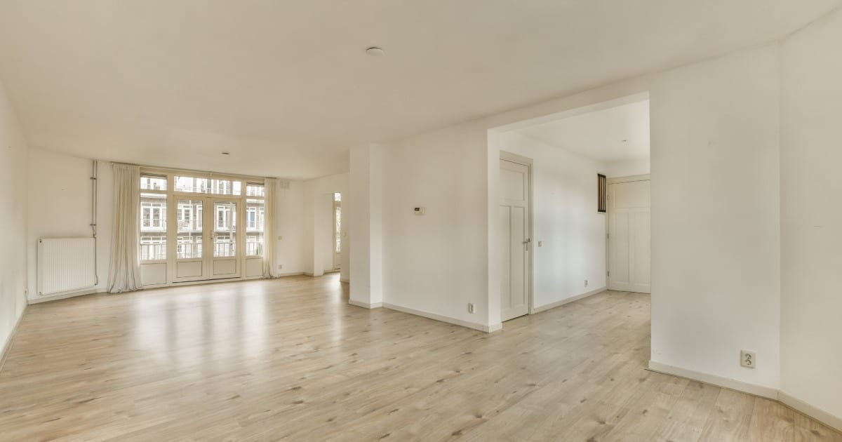 Un salon vide avec parquet au sol et murs blancs dans la pièce est très propre.