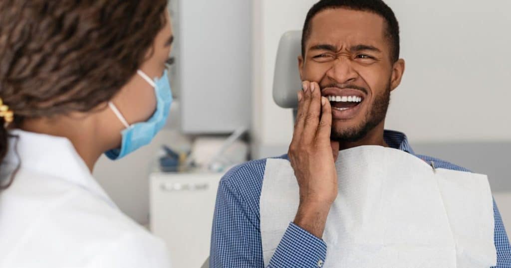 homme sur un siège de dentiste avec un mal de dent et une dentiste avec un masque