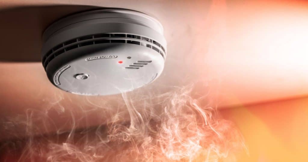 Zoom sur un détecteur de fumée située sur un plafond, avec de la fumée qui arrive jusqu'à lui. 