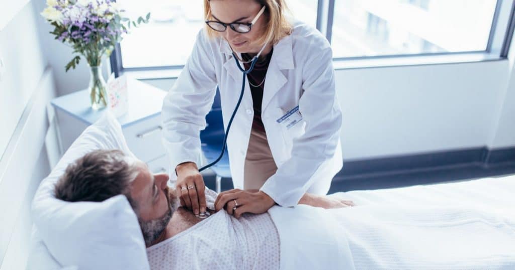 Une docteur en blouse blanche examine un patient sur son lit d'hôpital à l'aide d'un stéthoscope. 