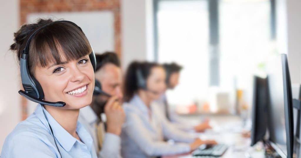 4 employés en chemises face à leurs ordinateurs avec des casques et micro dans un call center