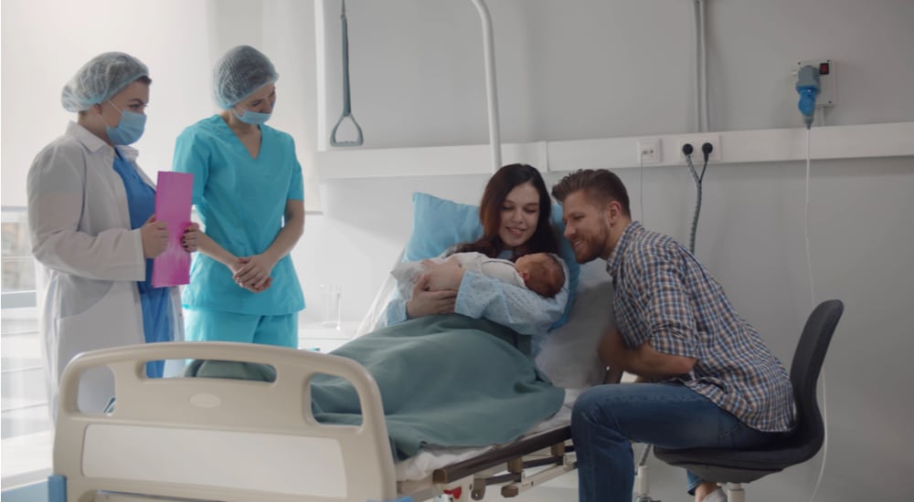 Couple dans une chambre de la maternité, avec leur bébé et deux femmes du corps médical. 