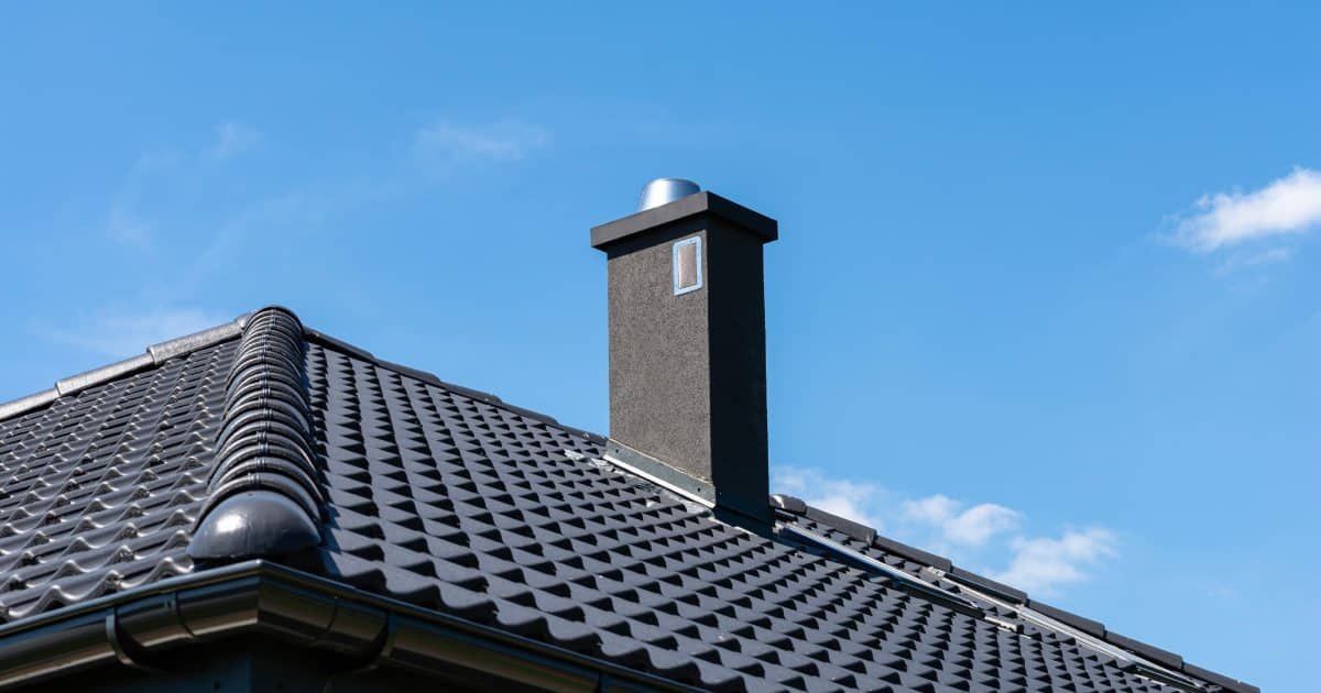Toit moderne sombre avec carreaux de céramique, gouttière et cheminée sous un ciel bleu clair.