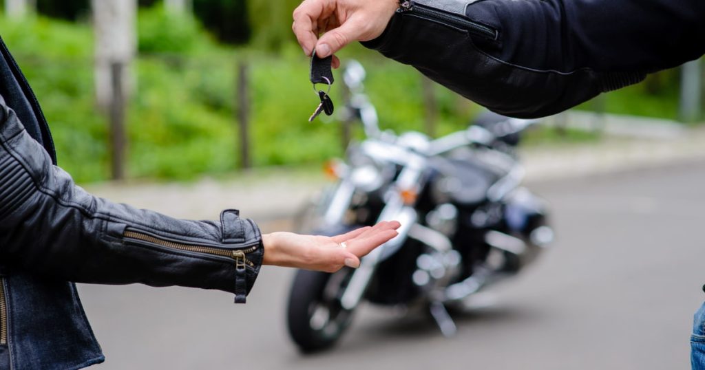 une main tendue et une autre qui donne une clé avec en arrière plan une moto et de la verdure