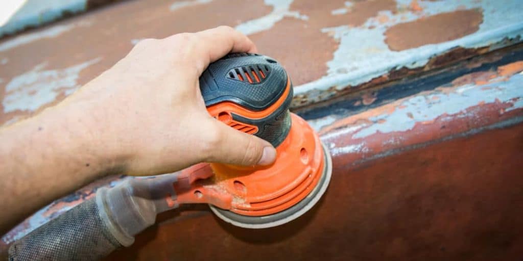 Main d'homme qui utilise une décapeuse sur une surface métallique