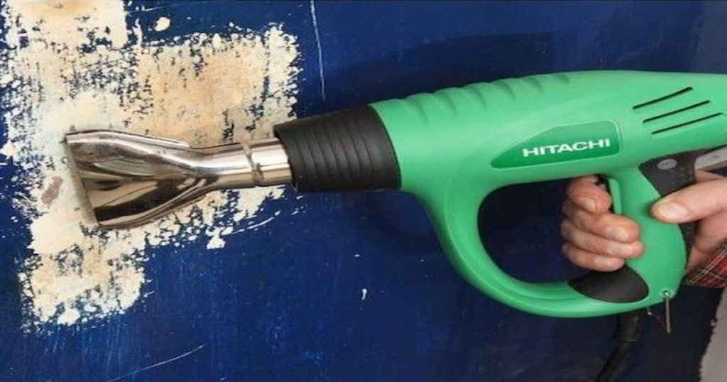 Main qui porte une machine pour décapage thermique verte sur un mur bleu