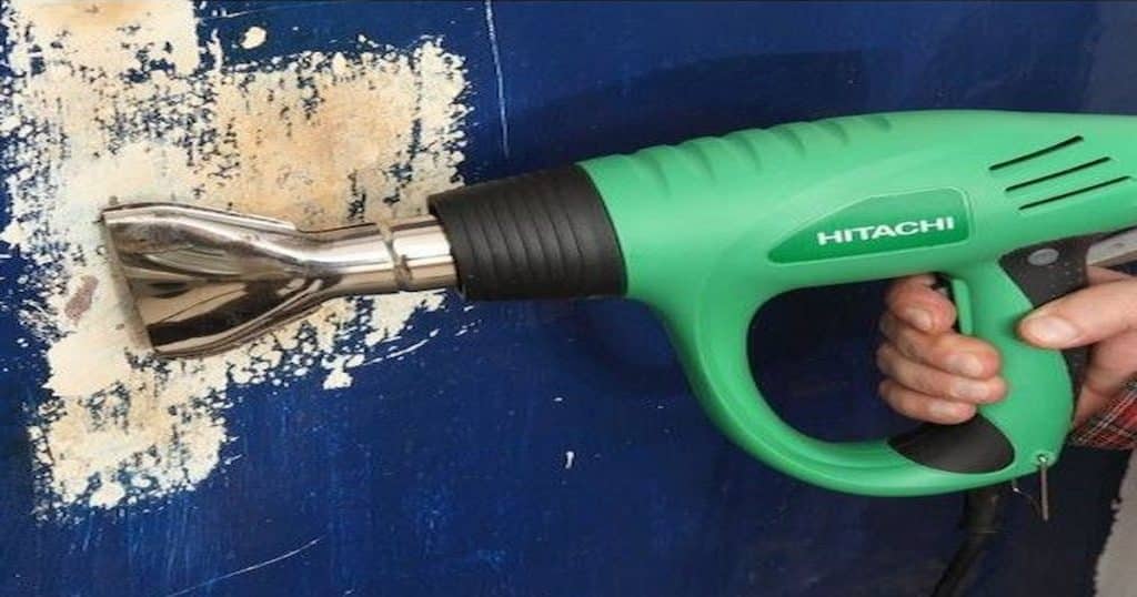 Main qui porte une machine pour décapage thermique verte sur un mur bleu