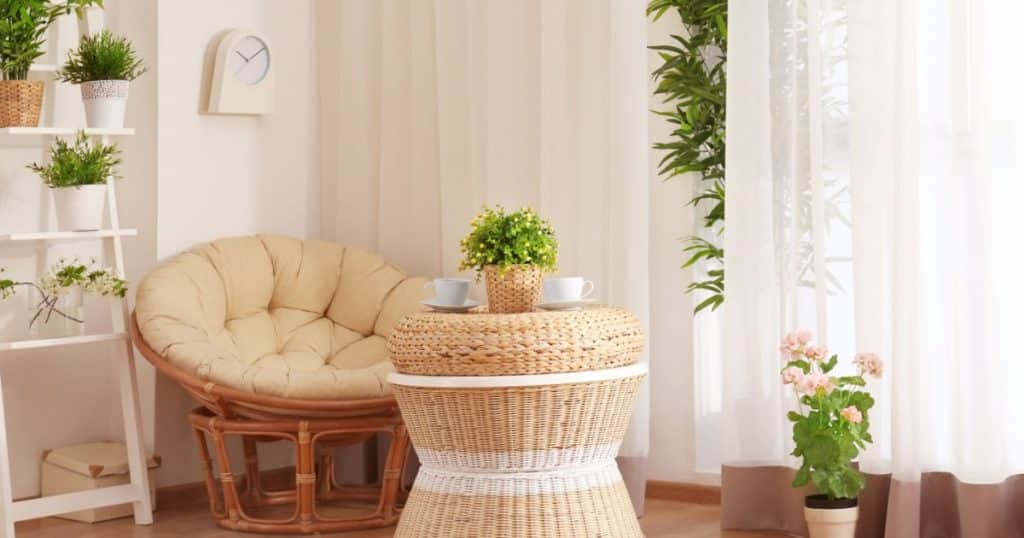 Intérieur d'une véranda décorée dans un style minimaliste et scandinave, dans des tons clairs, avec une table et un fauteuil en rotin, une étagère et de nombreuses petites plantes. 