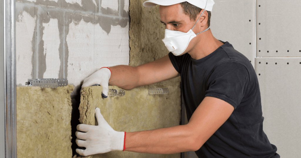 professionnel équipé d'un masque et de gants de protection, qui pose de la laine de verre sur un mur