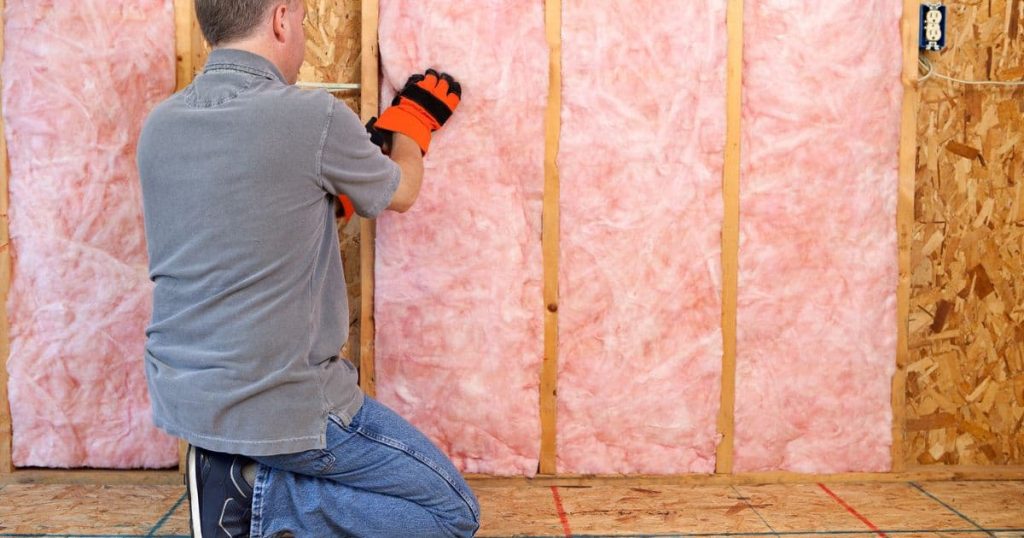 homme isolant mur de maison avec rouleaux rose d'isolant