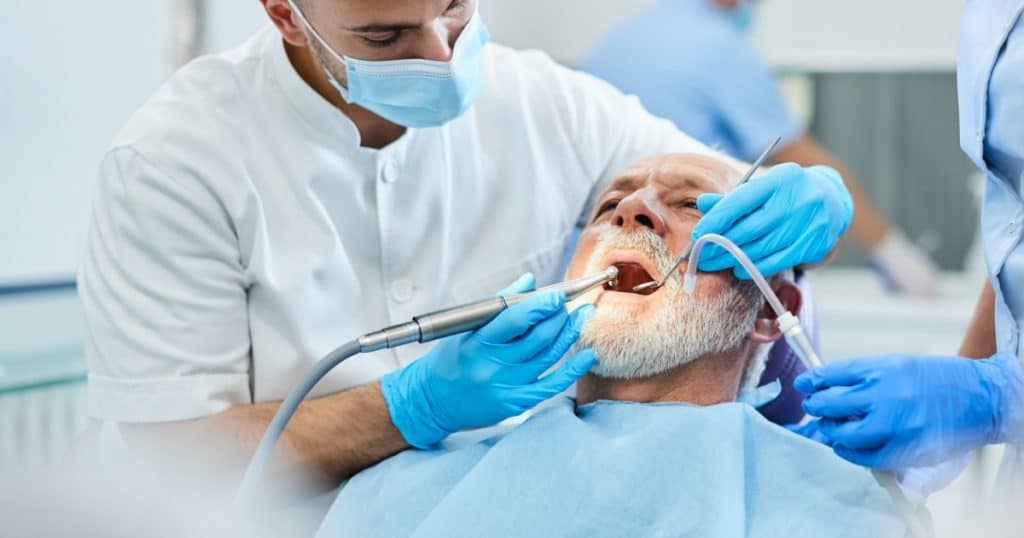 Un dentiste intervient sur les dents d'un homme âgé. 