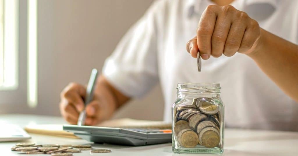 une personne qui met des pièces dans un bocal pour faire des économies