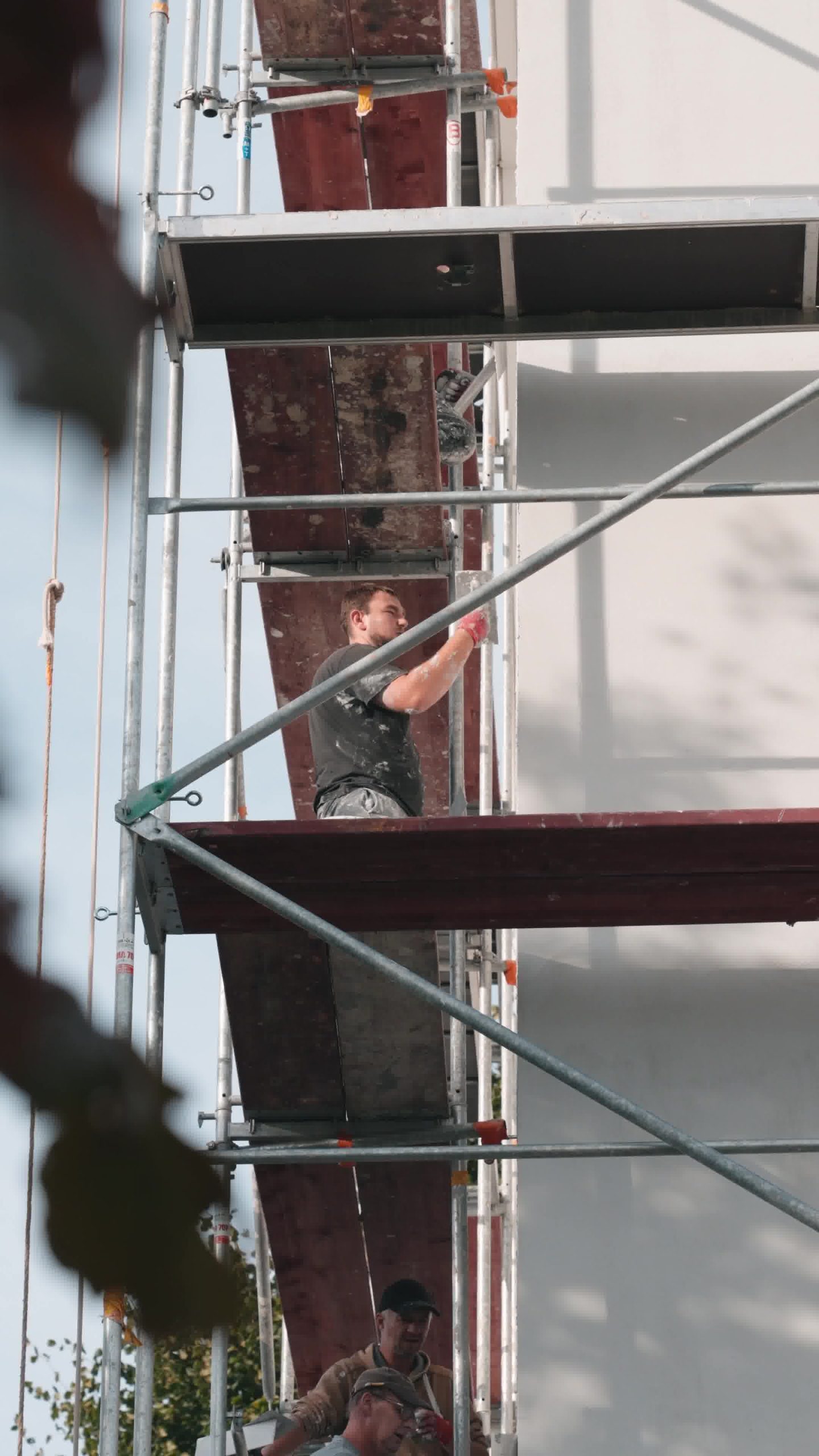 ouvrier sur un échafaudage en train d'enduire une façade de crépi à l'aide d'une taloche