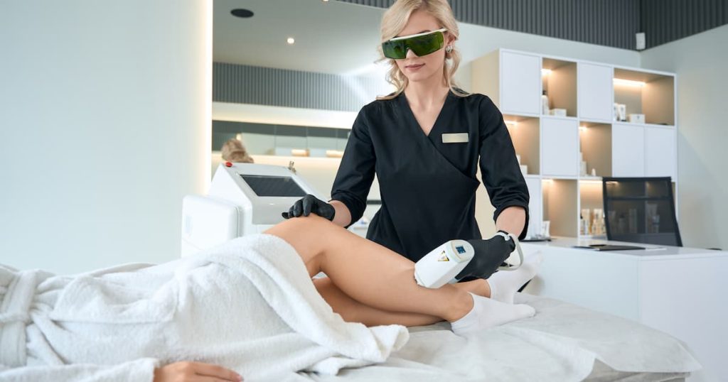 Esthéticienne qui pratique l'épilation laser sur les jambes d'une femme