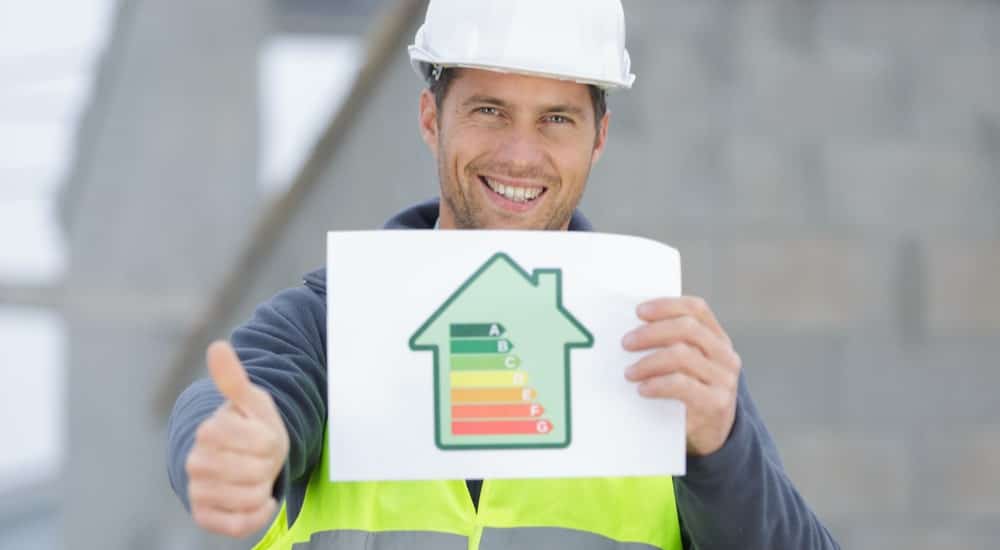 Homme habillé avec un gilet fluo et un casque de chantier, montrant une feuille avec une maison et les différents PEB. 
