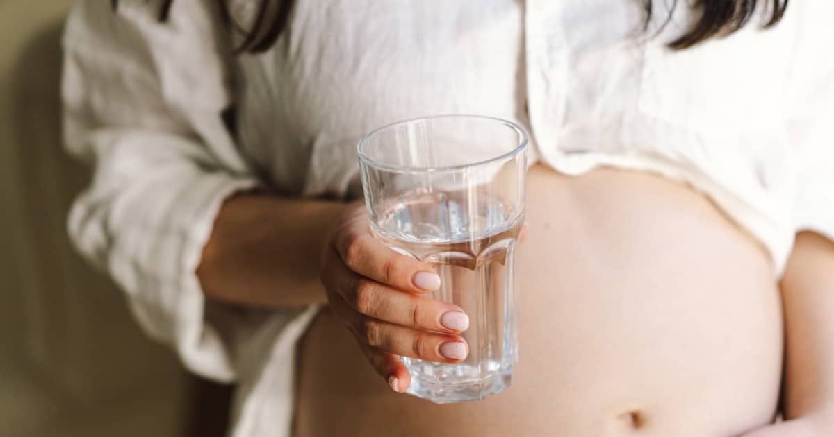 Femme enceinte tenant dans une main un verre d'eau.