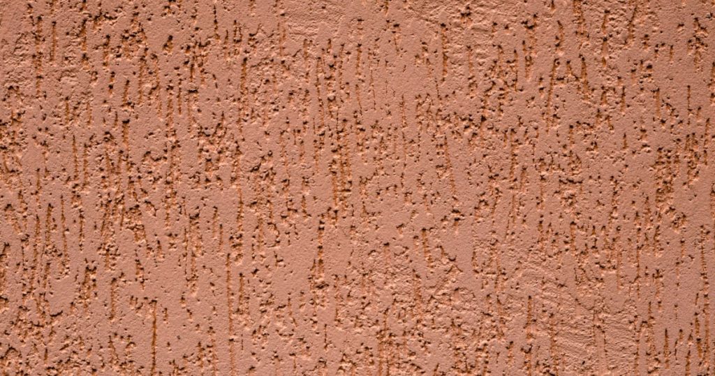 Zoom sur une façade extérieure en crépi écrasé couleur rouille.