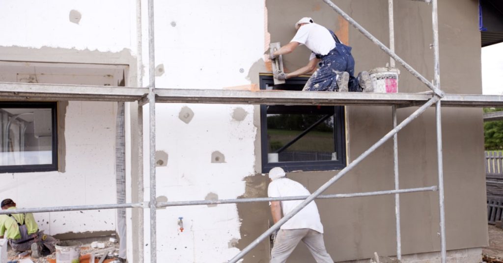 ouvriers en train de poser un enduit de finition sur un isolant de façade d'une maison