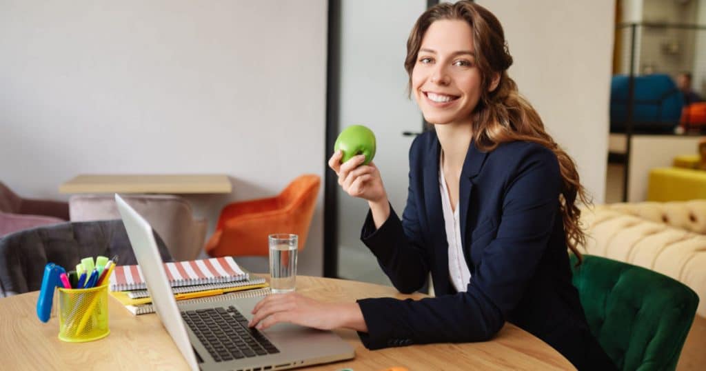 femme tenant une pomme dans sa main en train de travailler dans son entreprise sur son ordinateur