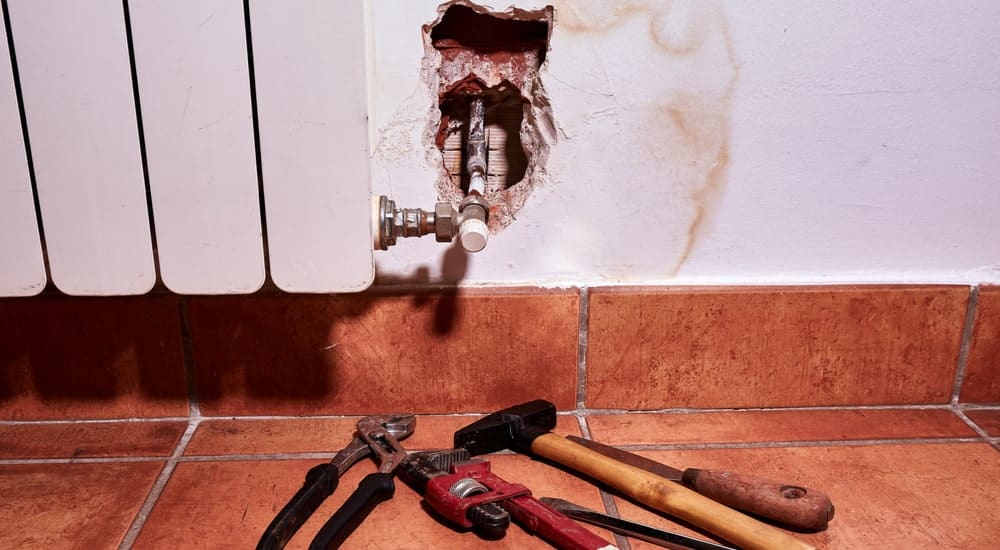 Dégâts sur le mur intérieur d'une maison suite à une fuite d'eau au niveau du système de chauffage. Outils disposés au sol.