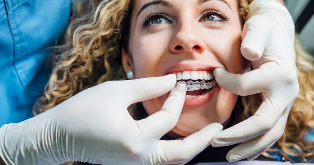 Deux mains d'un dentiste placent une gouttière dentaire sur les dents d'une jeune femme. 
