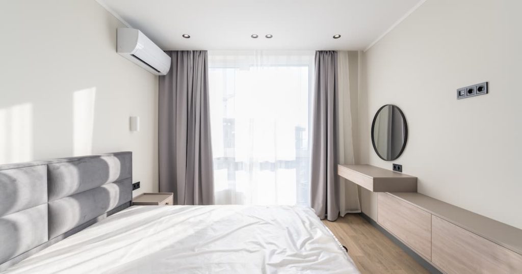 Grand coin de la chambre dans un style moderne avec un grand lit, une fenêtre, la climatisation et un miroir rond