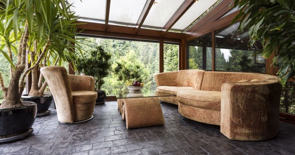 un salon composé de canapé, d'un fauteuil et de plantes dans une véranda lumineuse