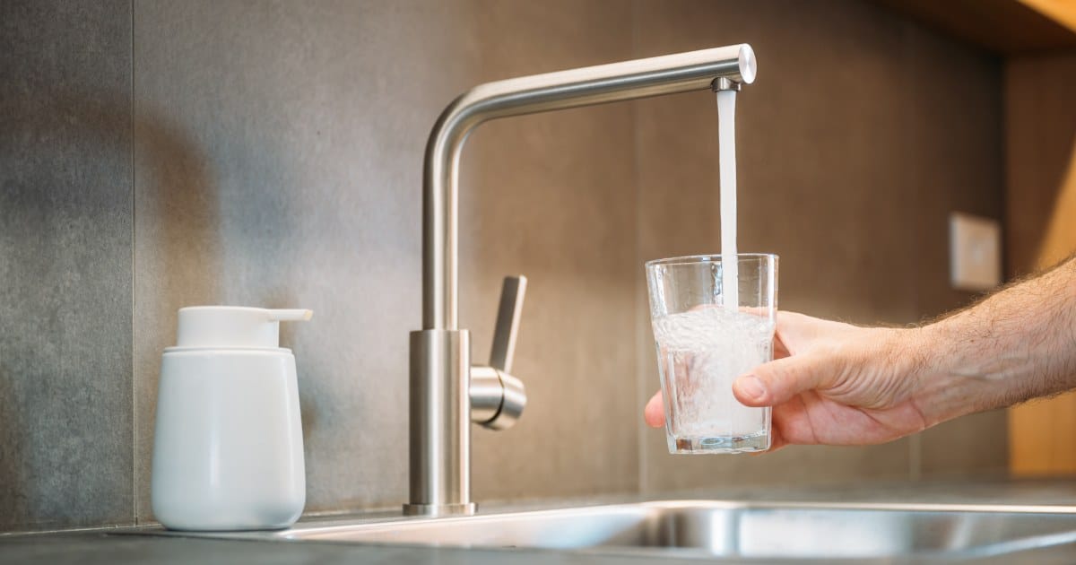 Une homme se servant un verre d'eau adoucie par un adoucisseur se trouvant sous l'évier.