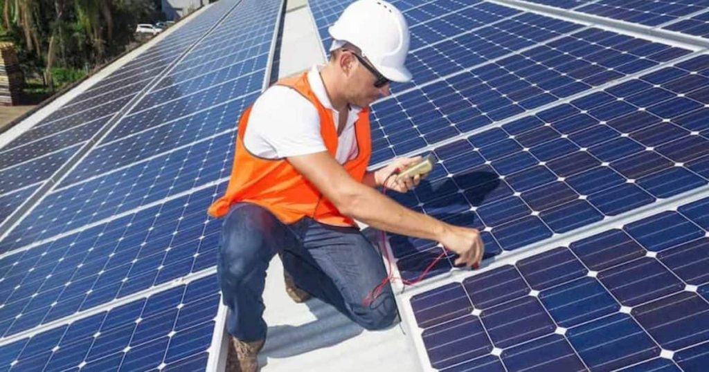 Homme avec casque blanc et chasuble orange travaille sur le toit rempli de panneaux solaires