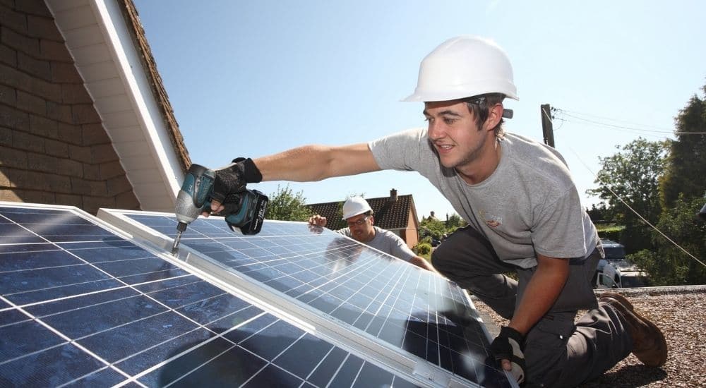 Un installateur de panneaux solaires en train de fixer les panneaux sur un toit plat.