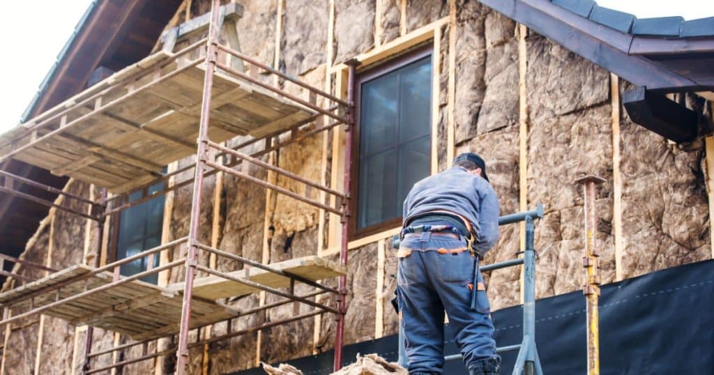 Isolation thermique d'une façade par un ouvrier sur un échafaudage avec de la laine de verre