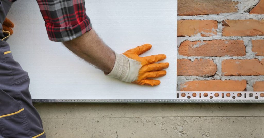 Homme qui pose une plaque d'isolant sur un mur extérieur