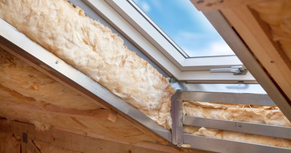 L'intérieur d'un rampant de maison avec une fenêtre de type Velux au milieu pendant sa phase d'isolation à la laine de verre.