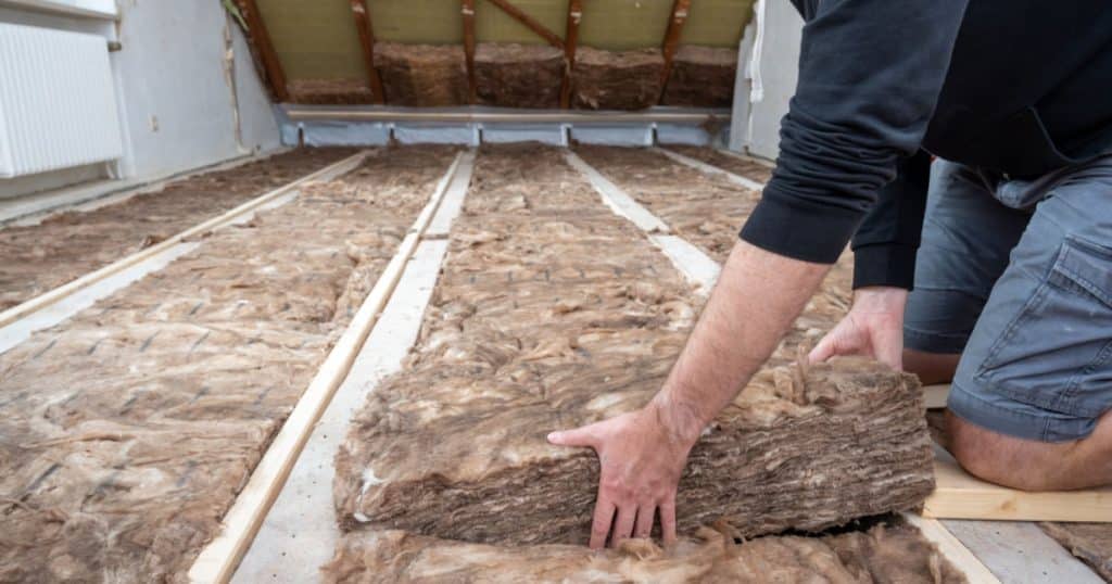 Une personne pose de la laine de roche dans les combles d'un bâtiment