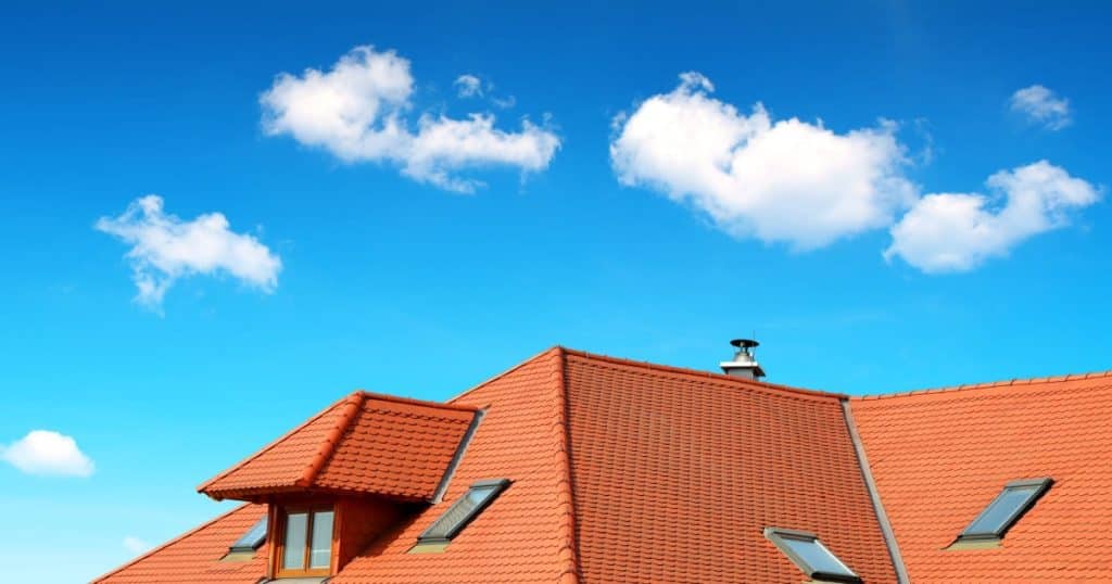 Le toit en tuiles rouges d'une maison se dégage sur un ciel très bleu avec quelques nuages. 