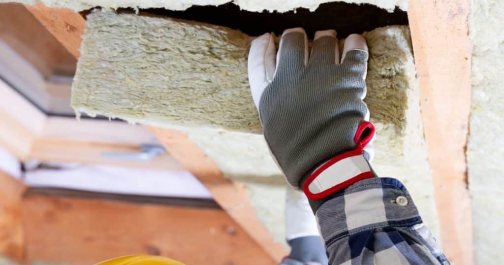 La main gantée d'un ouvrier isole le toit d'une habitation avec un morceau de laine de roche. 