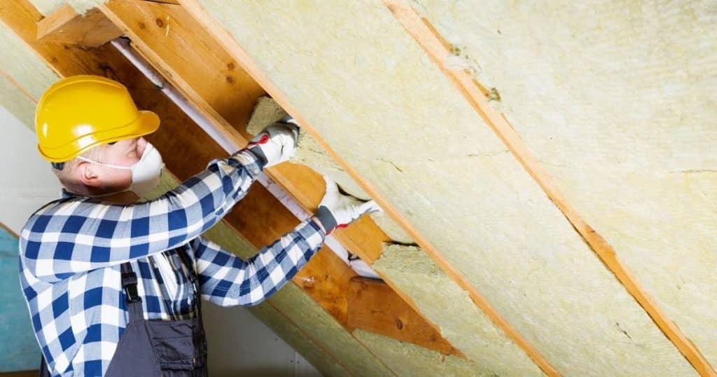 Isolation d'une toiture intérieure avec panneaux de fibre de bois par un professionnel portant un casque jaune et des gants
